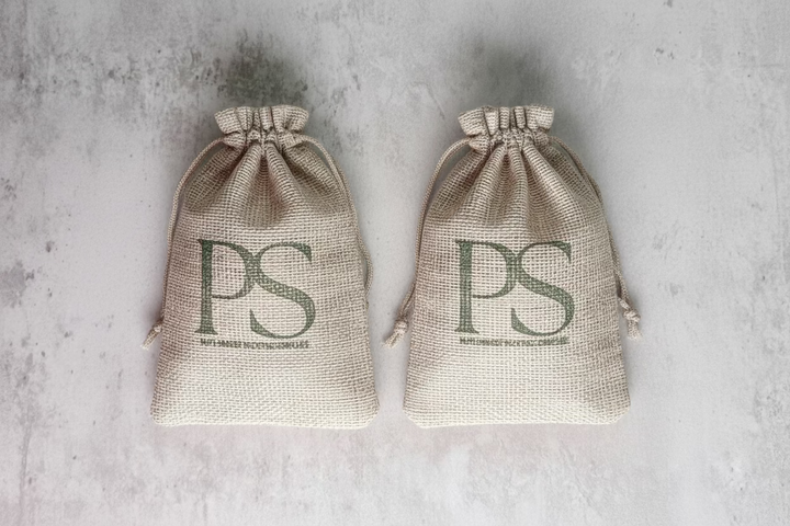 Two burlap sacks with 'PS' monogram, displayed on a stone surface, likely containing the soap sacks for shoe freshening.